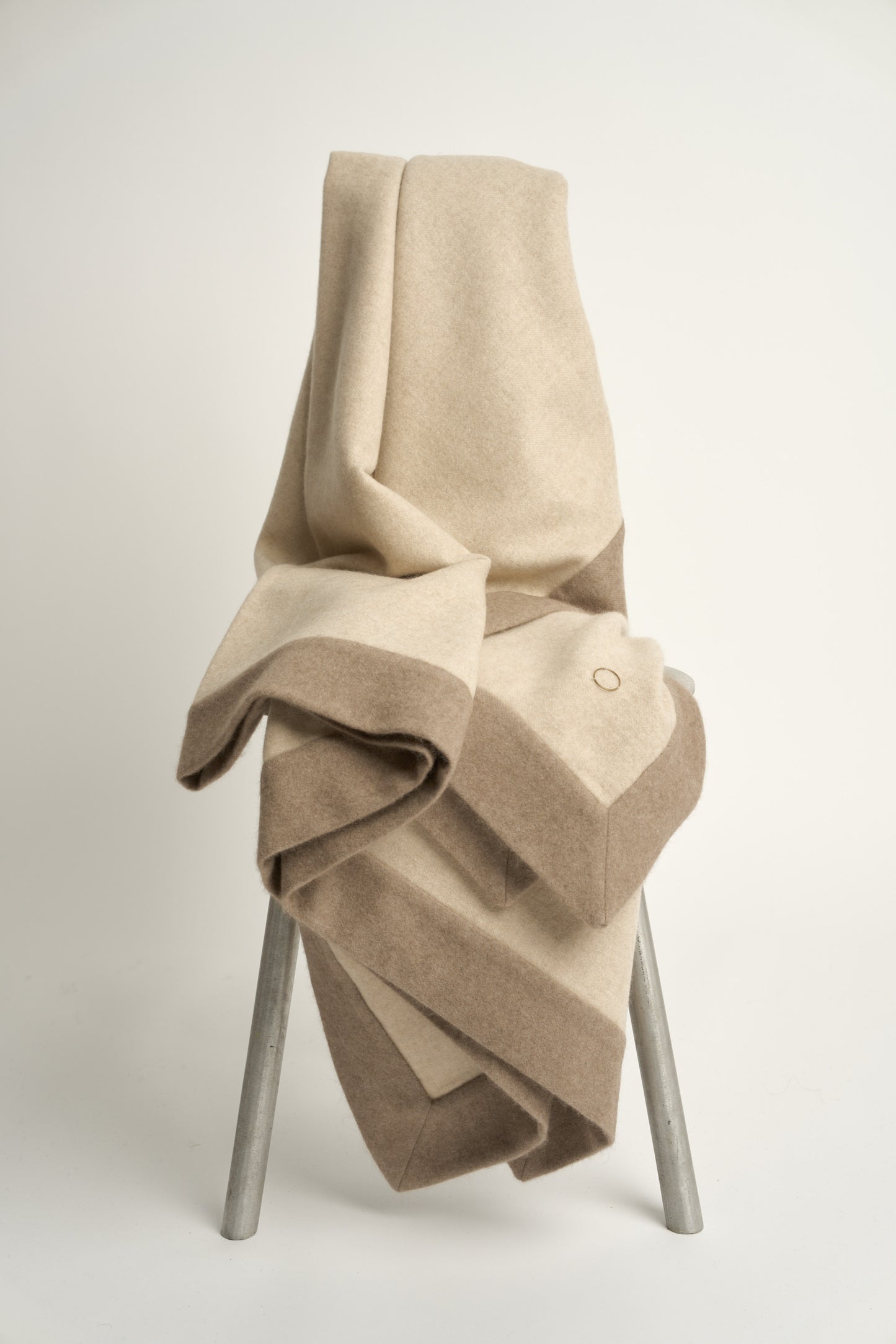 A beige and taupe etra throw blanket with a subtle pattern, draped over a chair with a white background