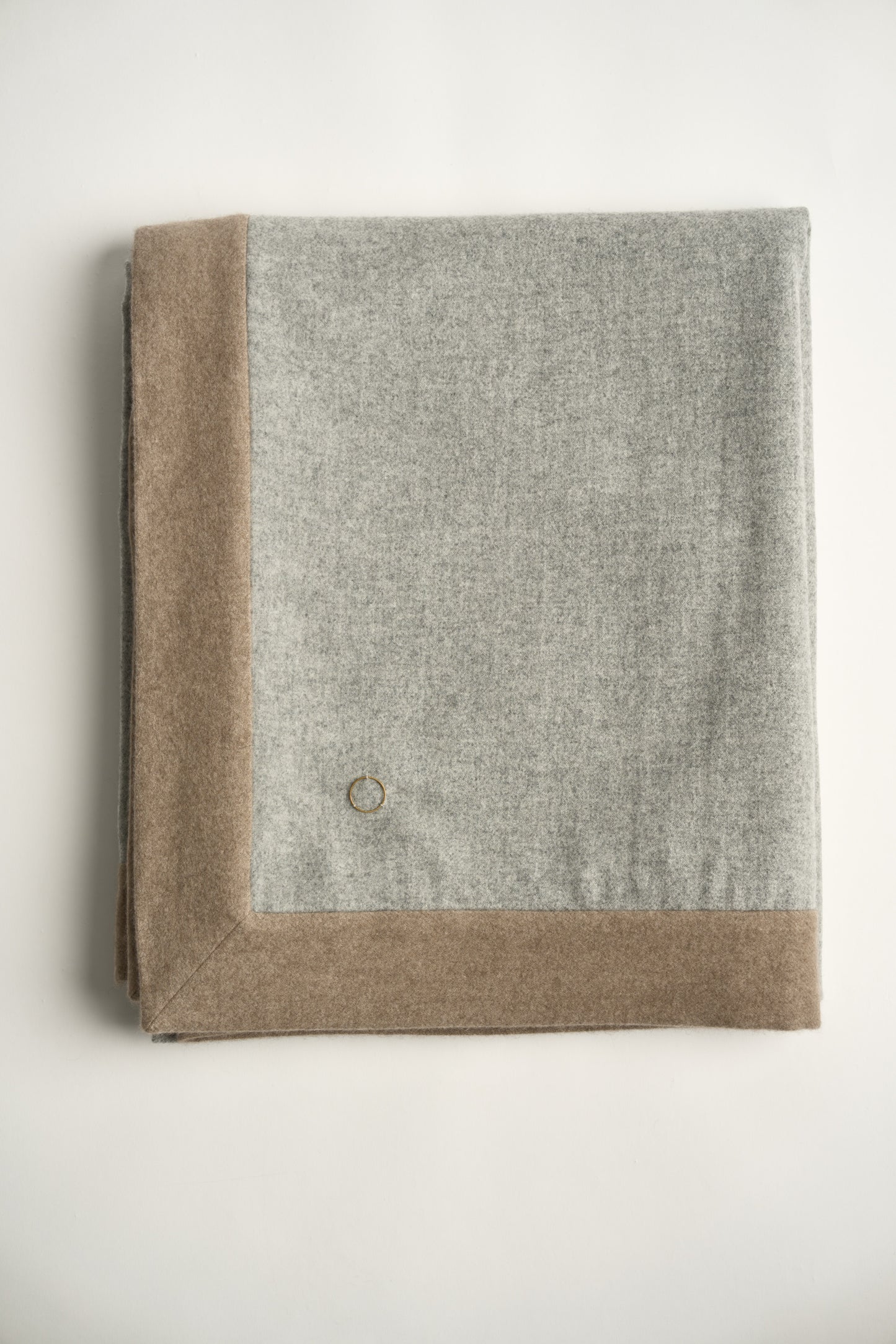 A soft grey & taupe etra throw blanket with a subtle pattern, draped over a chair with a white background