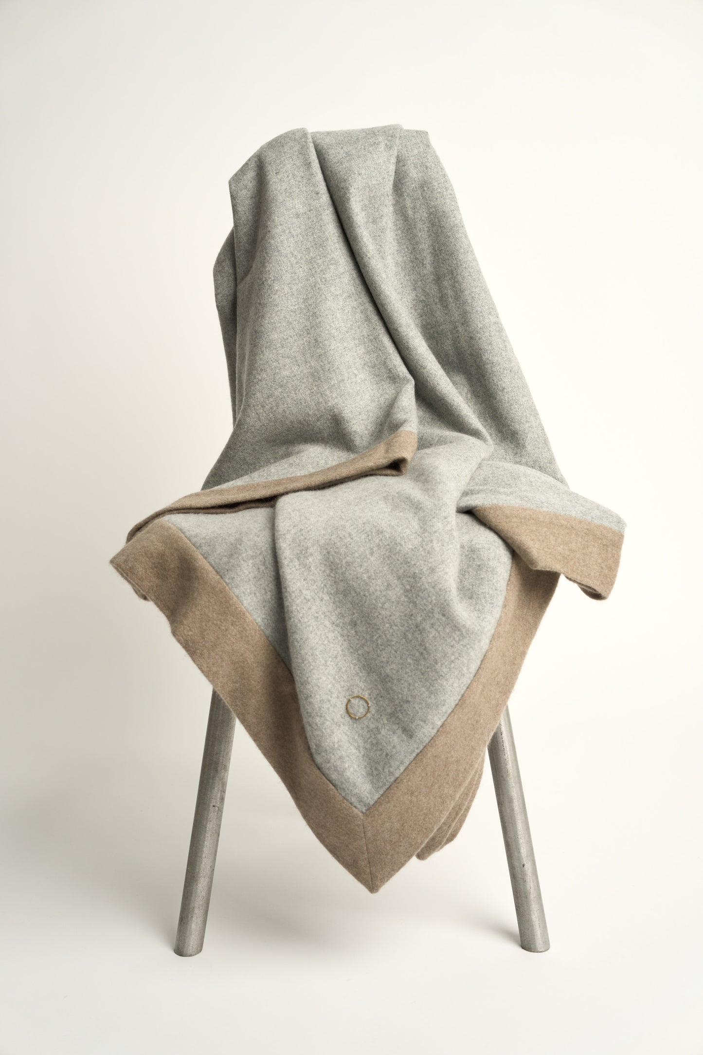 A soft grey & taupe etra throw blanket with a subtle pattern, draped over a chair with a white background
