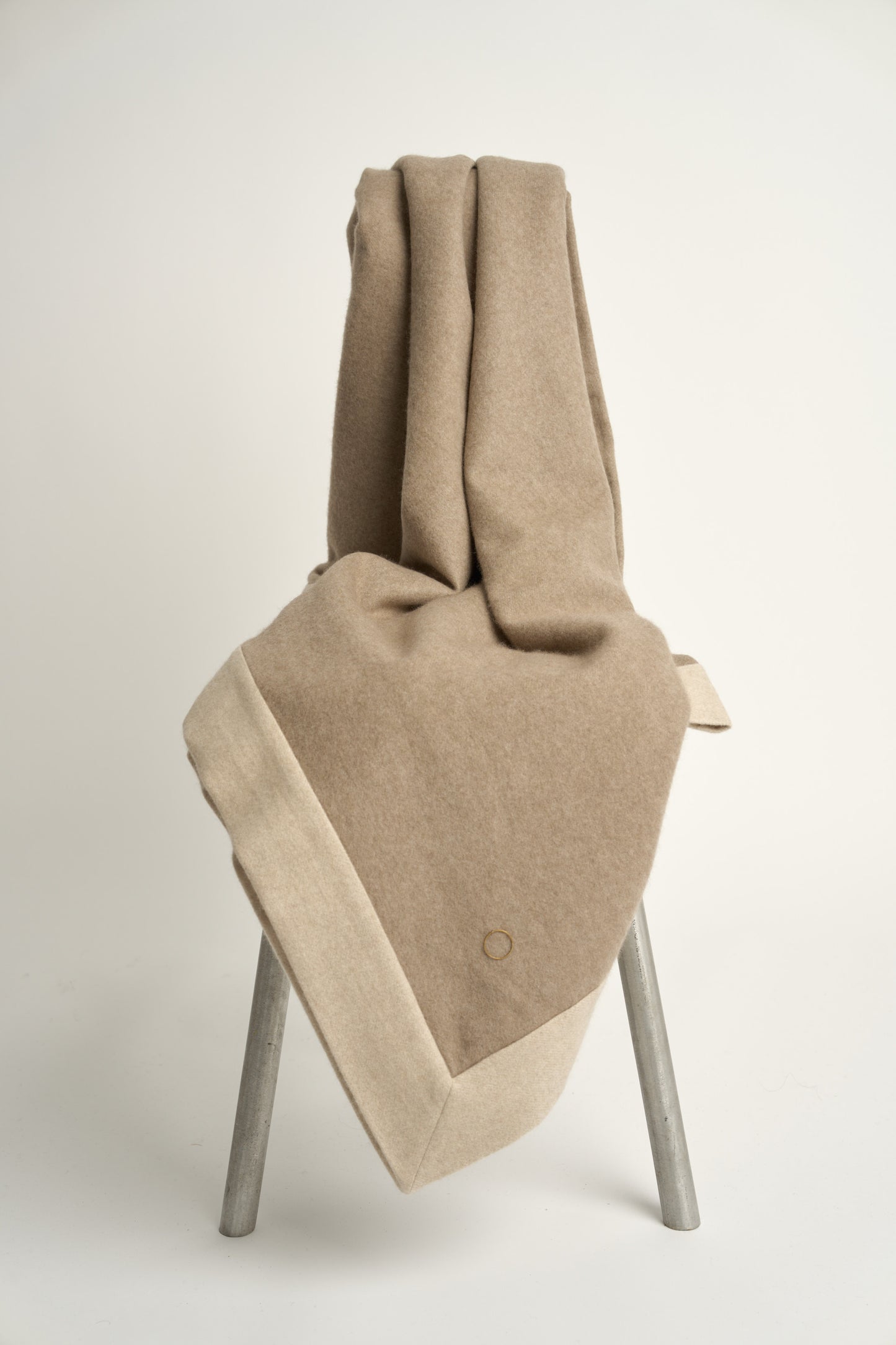 A taupe and beige etra throw blanket with a subtle pattern, draped over a chair with a white background