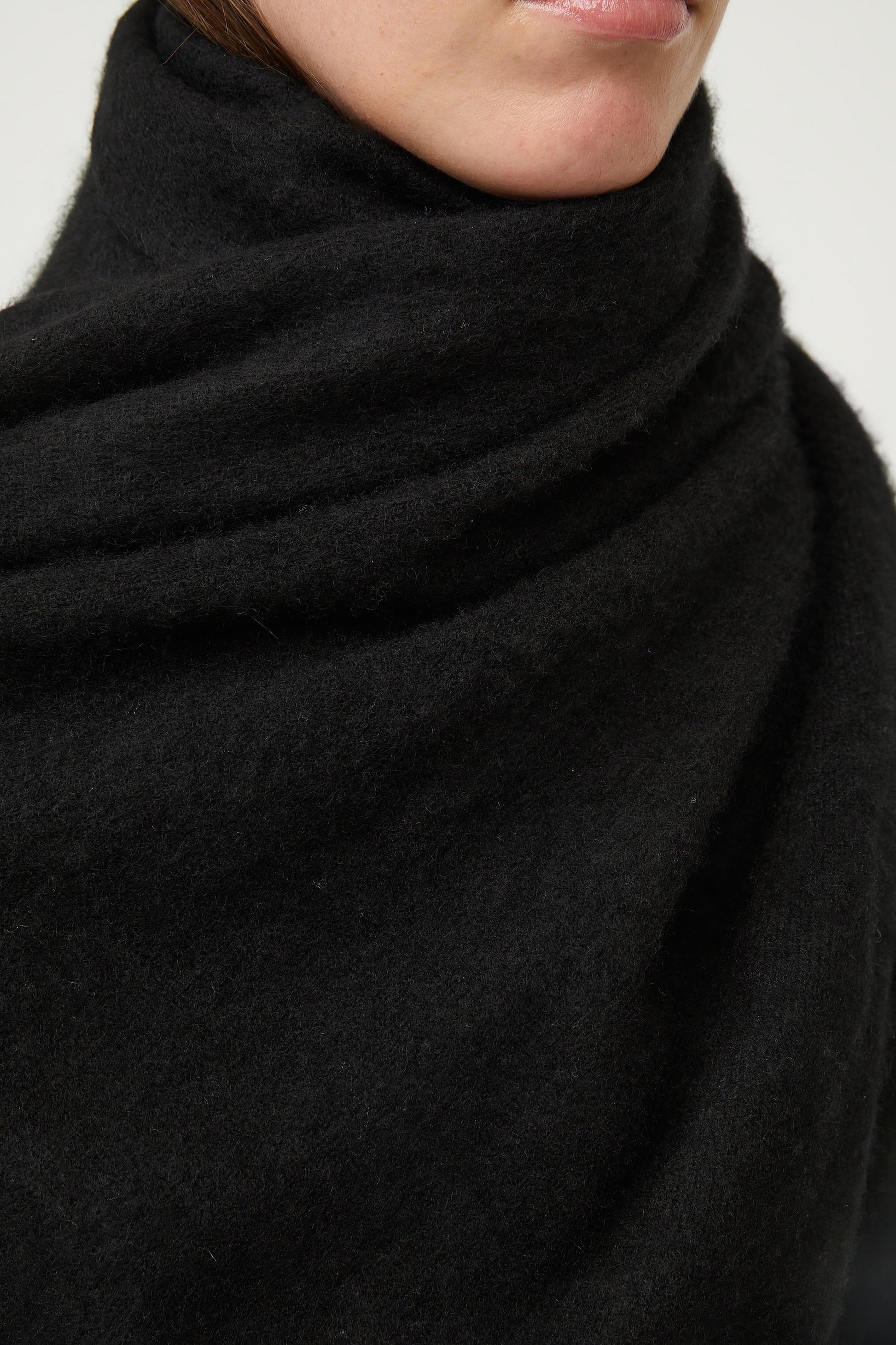 This image features the Feltra Shawl, an elegant and warm accessory made from felted cashmere, emphasizing pure simplicity and luxury. The shawl is presented in a deep, rich black color, enhancing its sophisticated and sleek appearance.