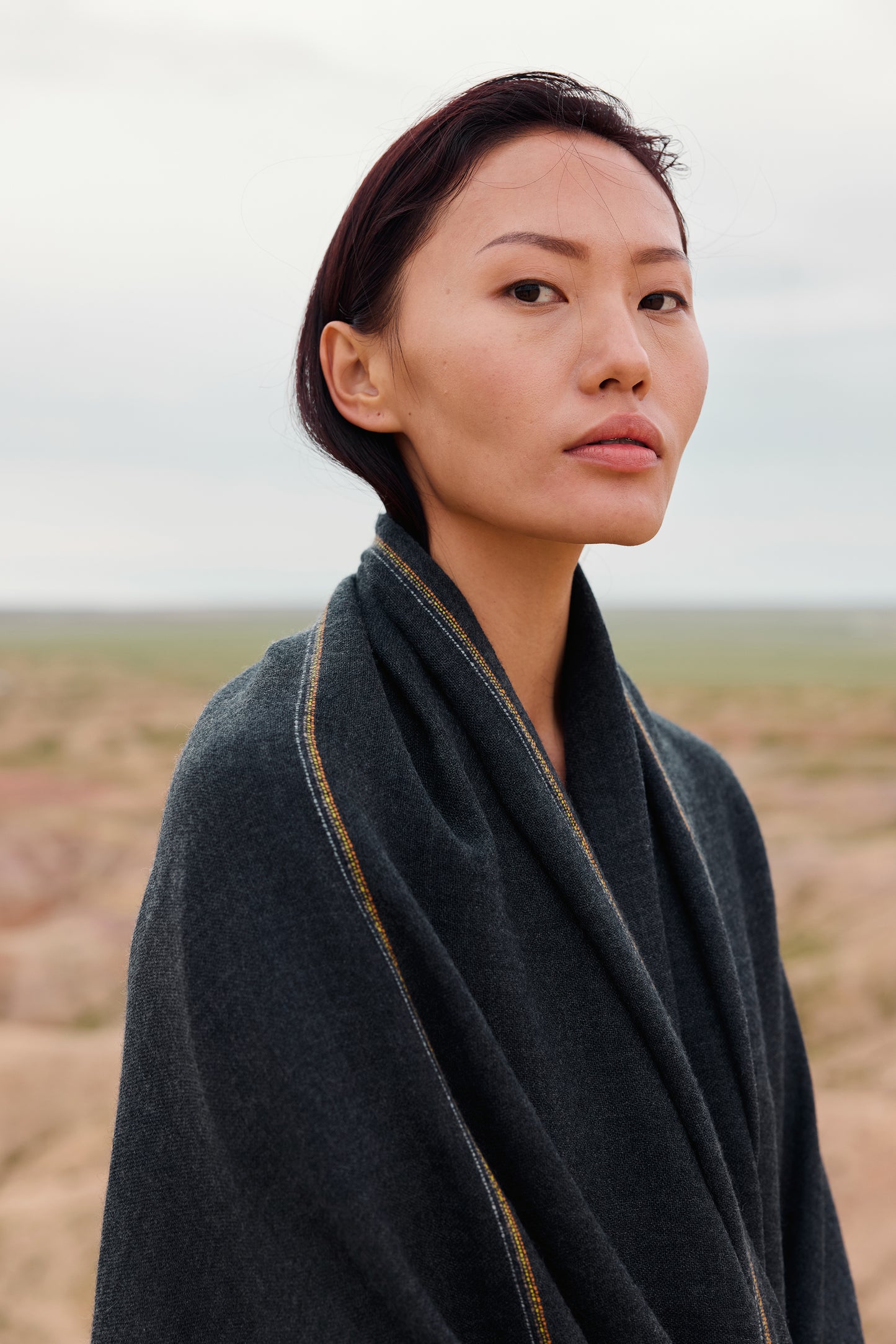 Close-up of a charcoal cashmere throw with contrast stripes and fringes.