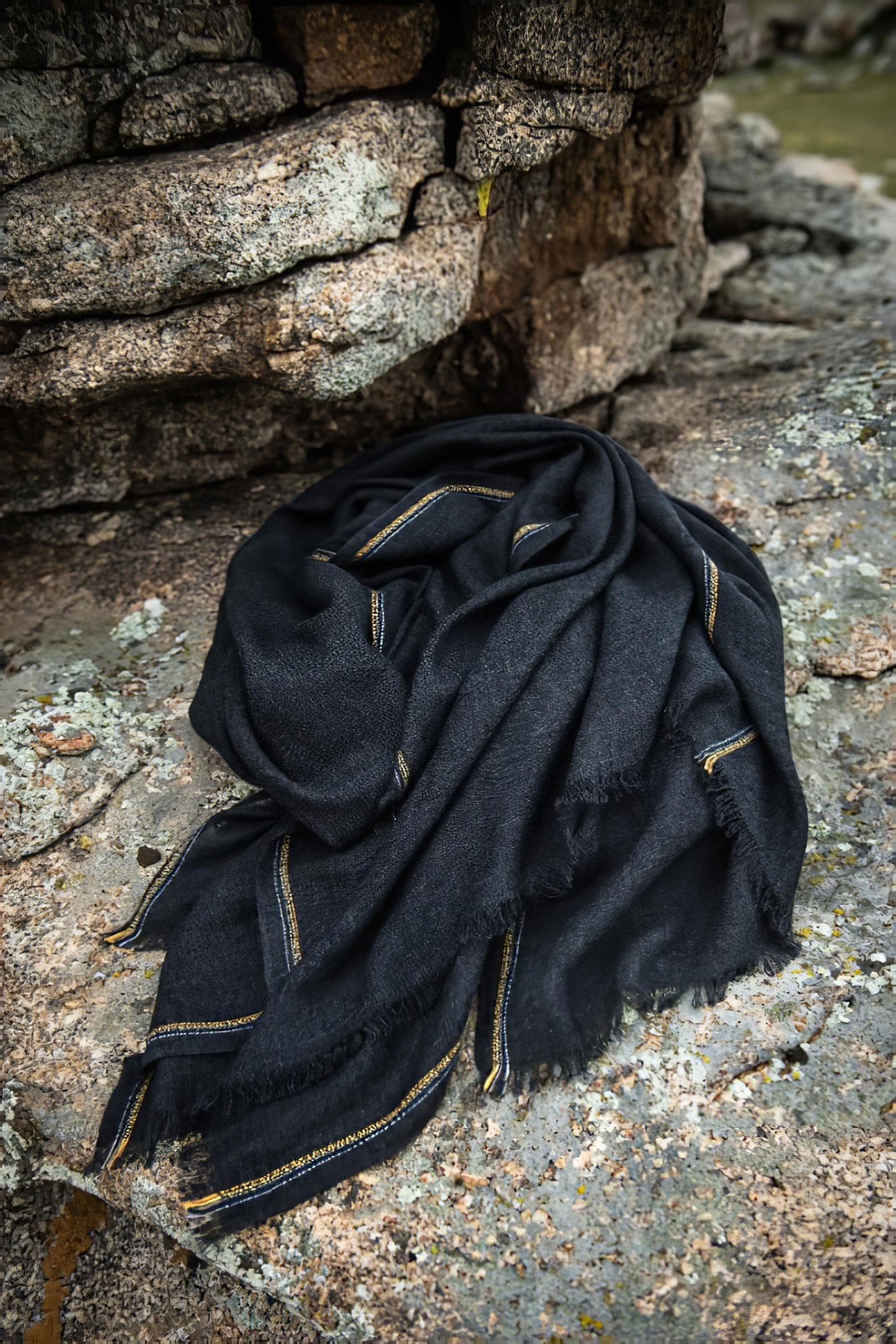 An image of a folded charcoal cashmere throw with contrast stripes and fringes.