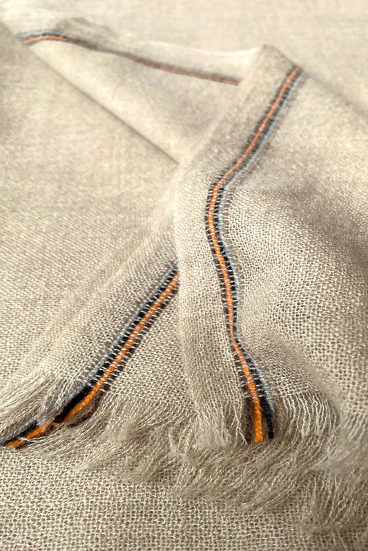 Close-up of a beige and brown cashmere throw with contrast stripes and fringes.