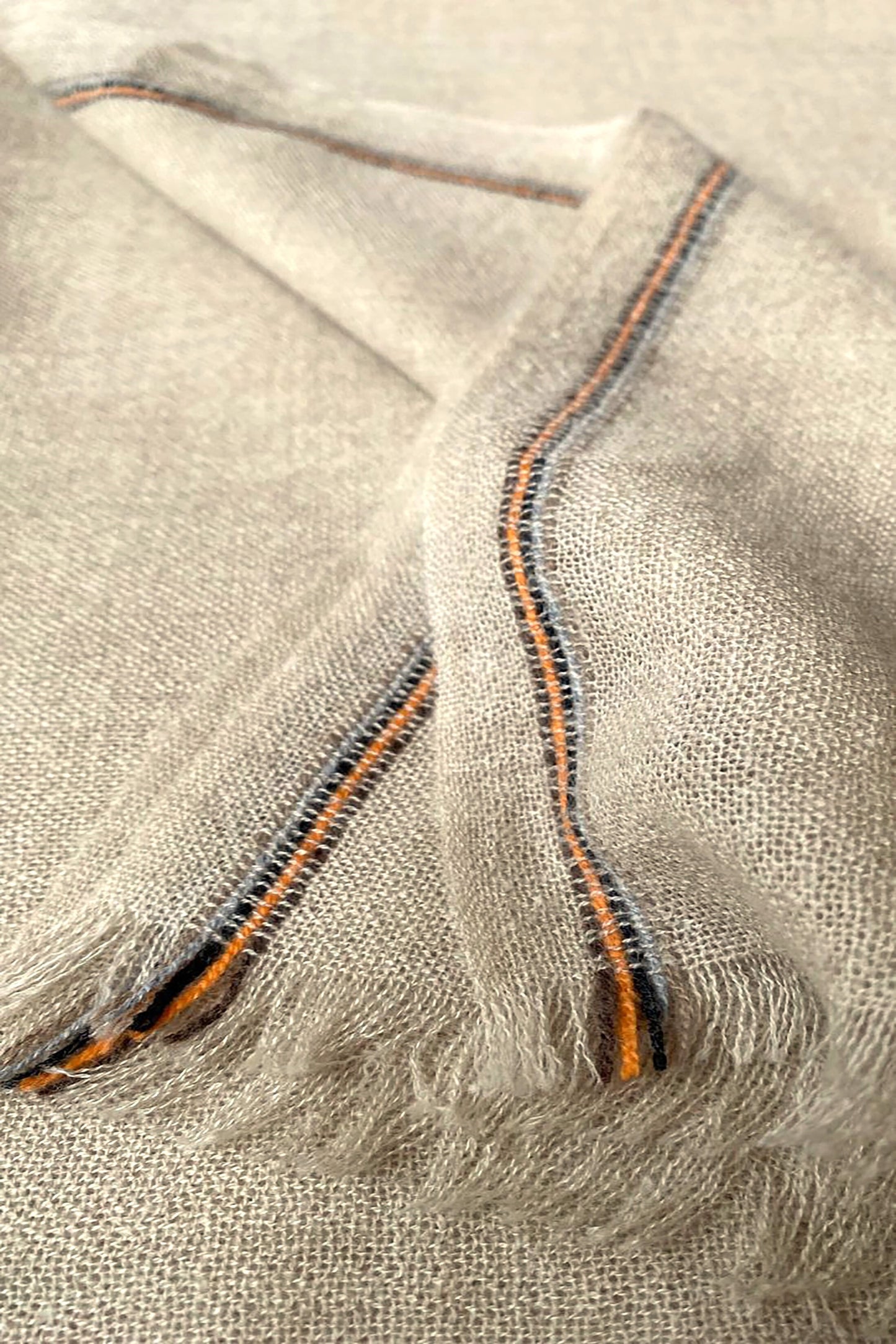 Close-up of a beige and brown cashmere throw with contrast stripes and fringes.