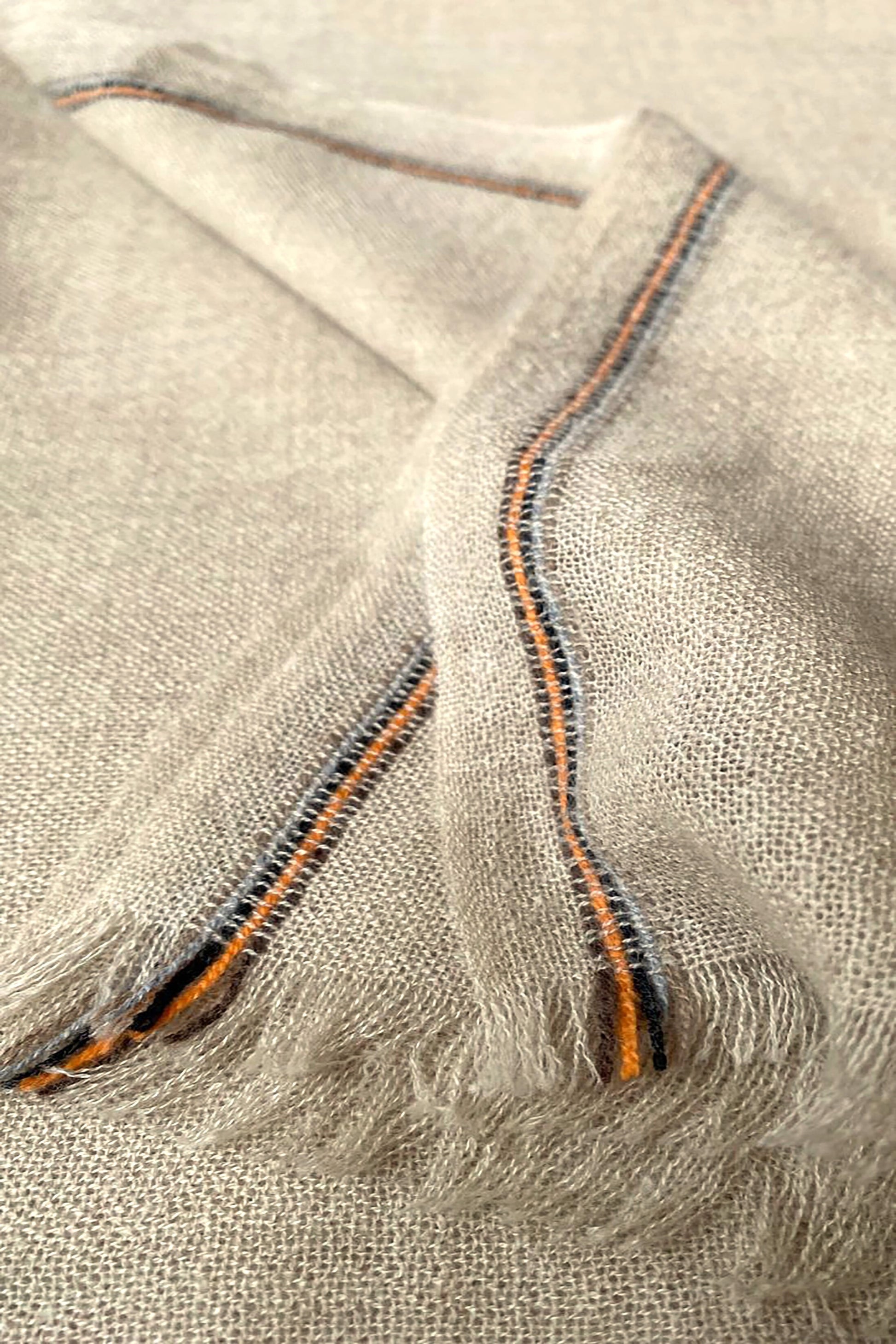 Close-up of a beige and brown cashmere throw with contrast stripes and fringes.
