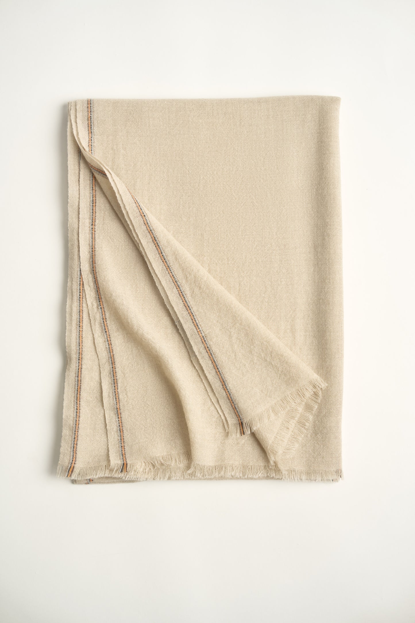 A folded beige-colored cashmere throw with visible contrast stripes and fringes on a light background.