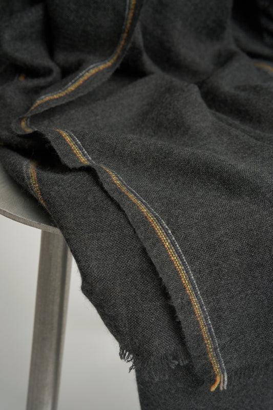 An image of a charcoal cashmere throw with contrast stripes and fringes draped over a chair.