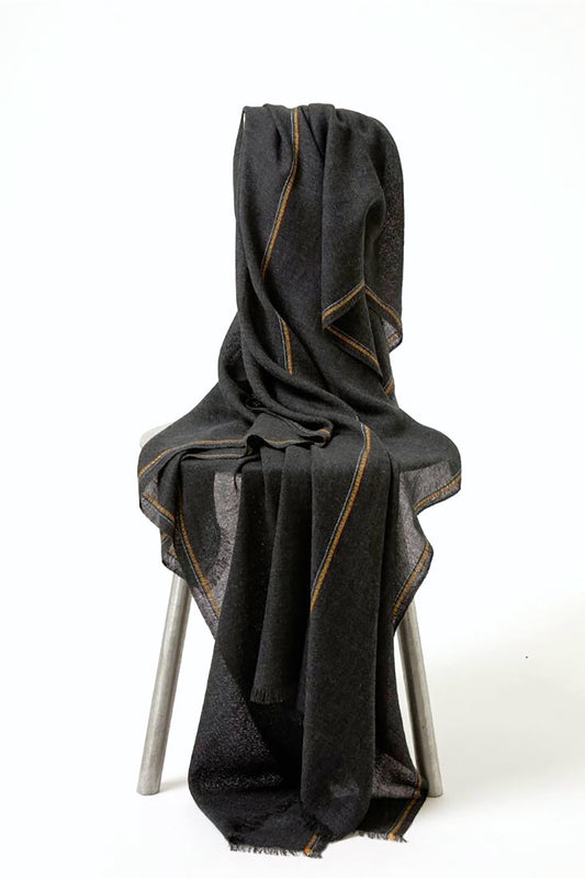 An image of a charcoal cashmere throw with contrast stripes and fringes draped over a chair.