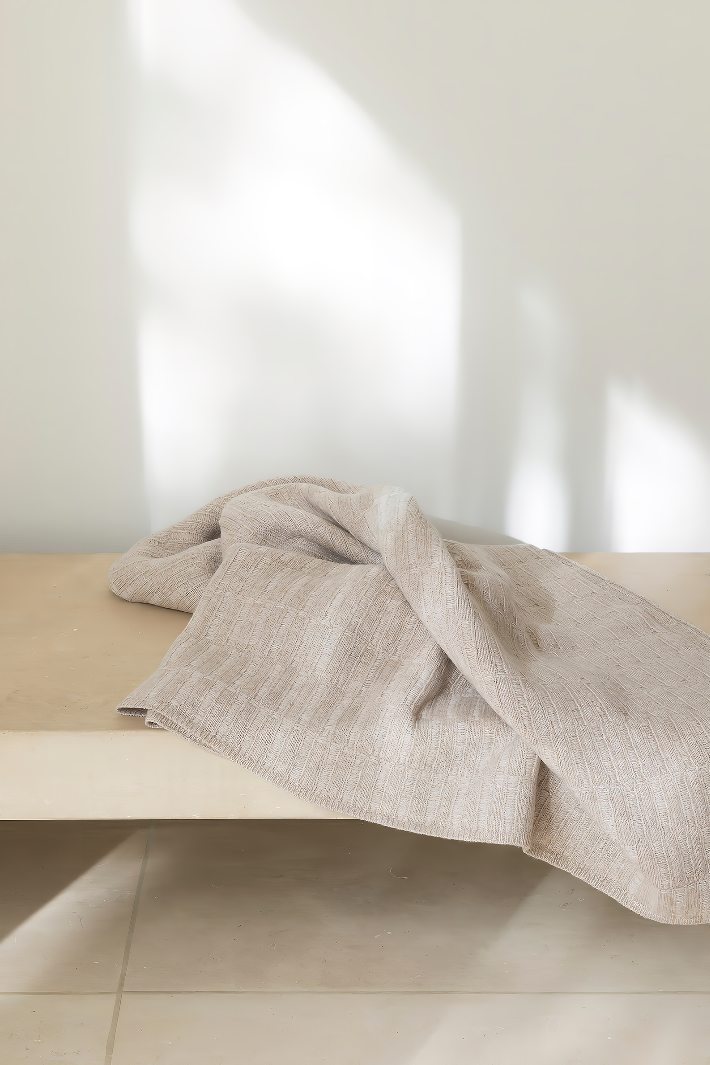 A feather throw blanket draped over the edge of a wooden bench, with a subtle textured pattern.