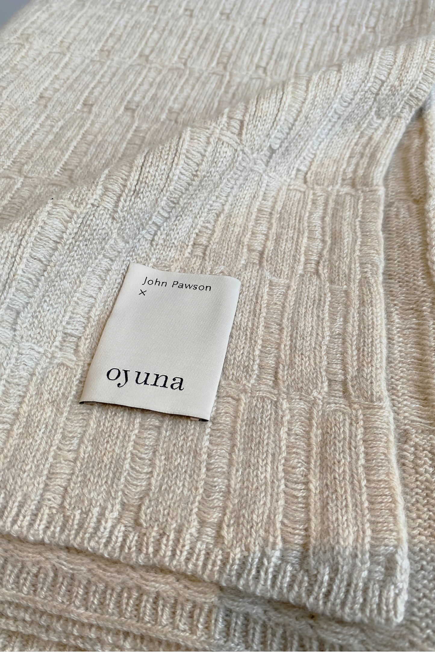 A flat lay image of the Lake throw in feather, showcasing the limited collection label