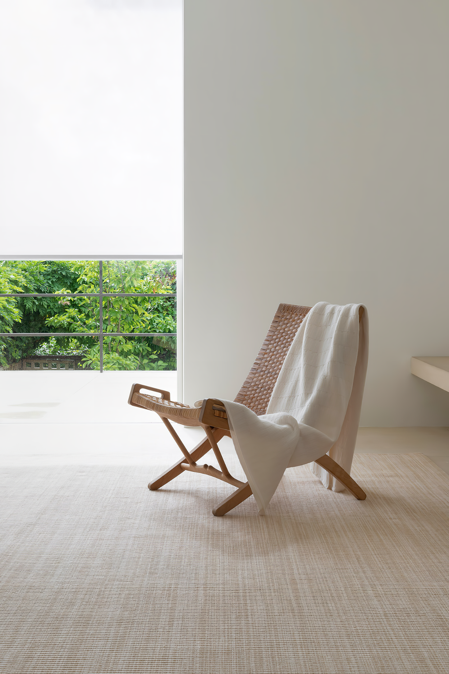 A room with a large window showcasing a natural outdoor scene. A ivory throw is draped over a chair in the foreground, with a subtle, textured pattern.