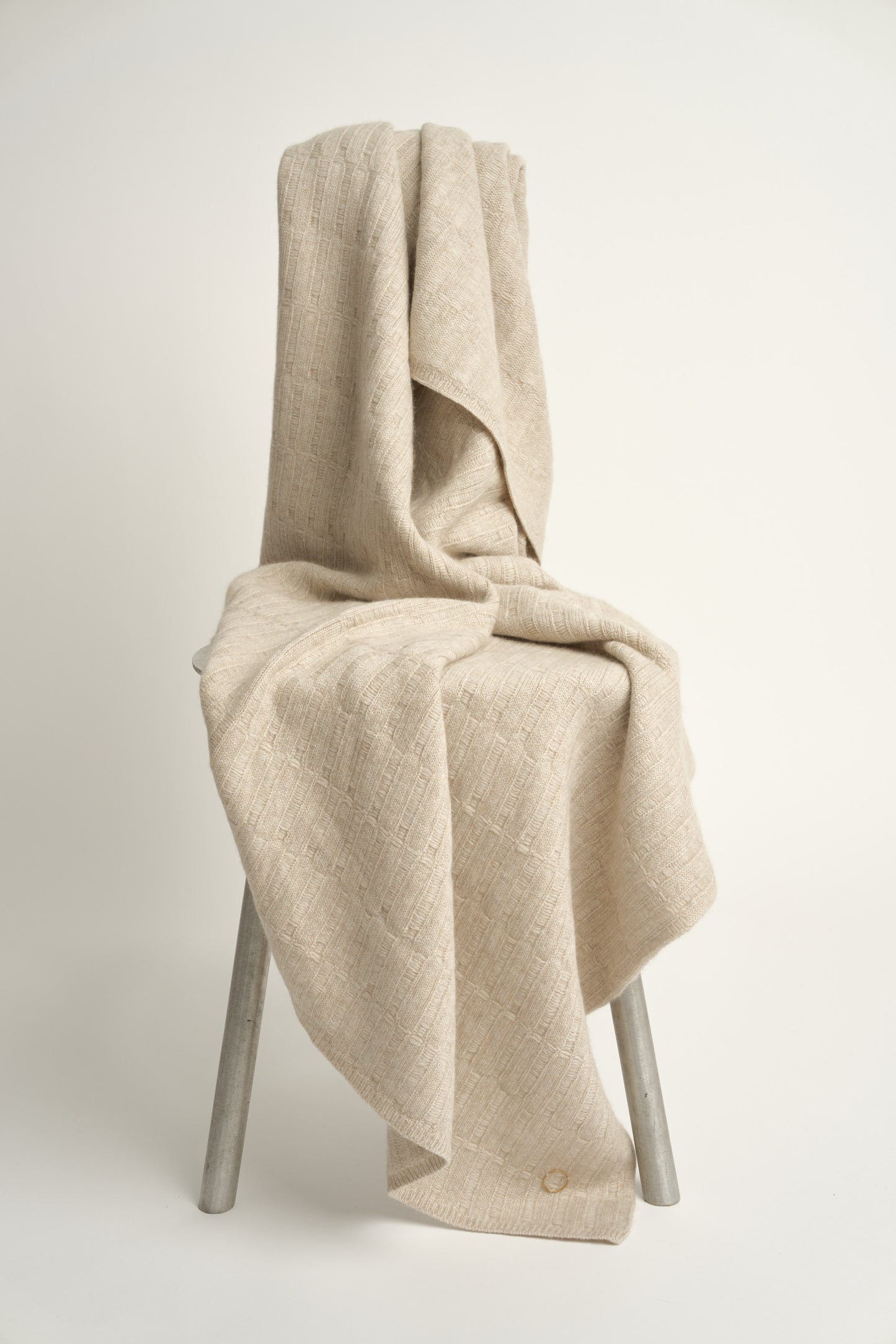 A feather throw blanket made of linen, draped over the back of a chair against a white background.