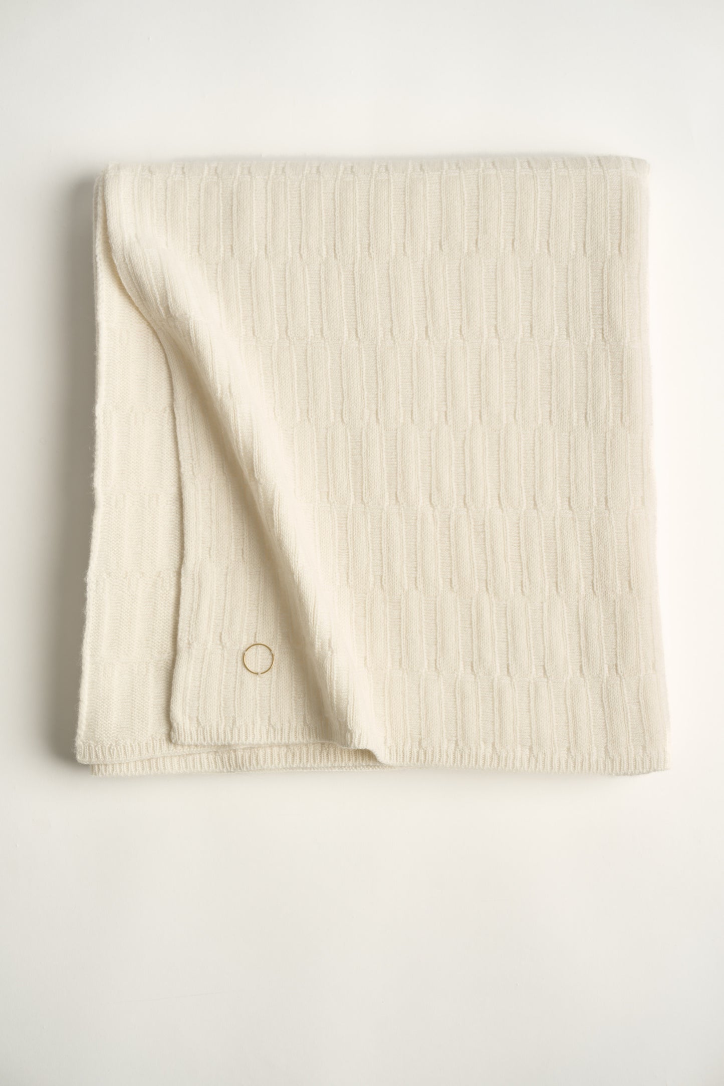 A folded ivory-colored throw blanket with a subtle textured pattern displayed on a white background.