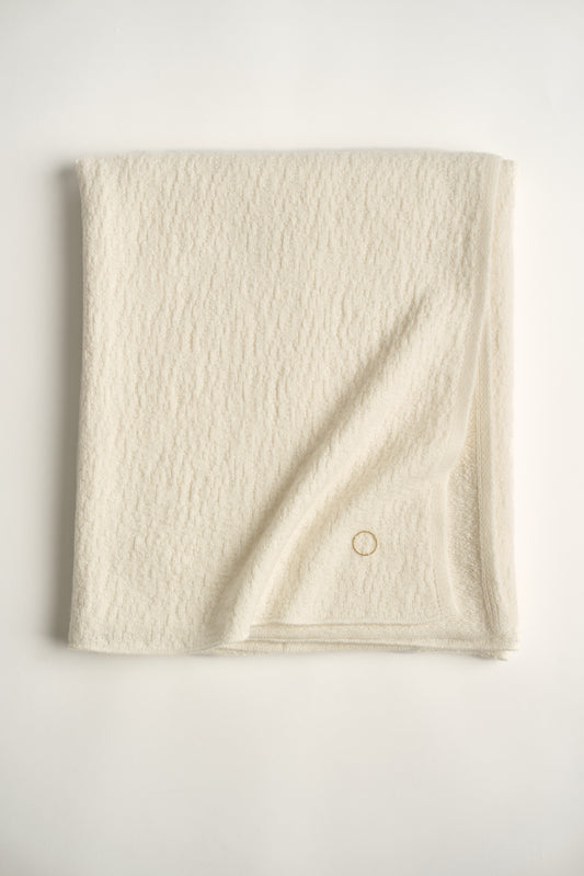 A folded luxurious and elegant ivory coloured throw draped over a chair