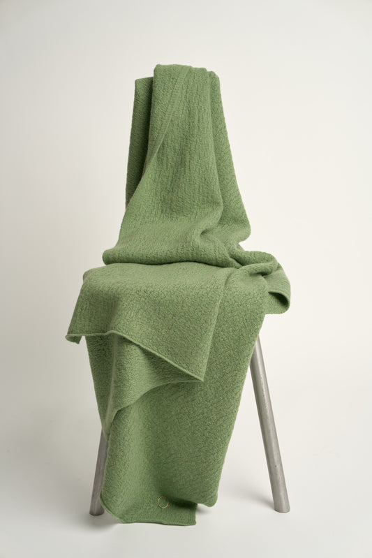 A green coloured soft throw draped over a chair
