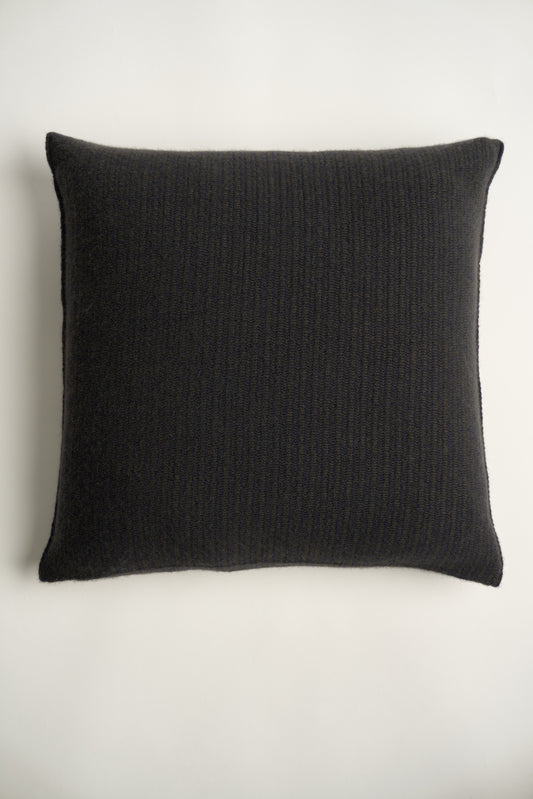 This image displays the Letra Cushion Cover, characterized by its knitted two-tone float knit design. The cushion cover features a textured, cozy appearance in a dark color, which comes across as modern and stylish.