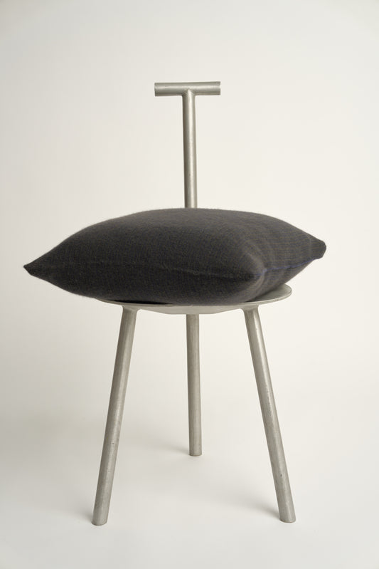 This image displays the Letra Cushion Cover, characterized by its knitted two-tone float knit design. The cushion cover features a textured, cozy appearance in a dark color, which comes across as modern and stylish.