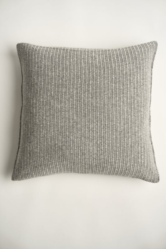 This image displays the Letra Cushion Cover, characterized by its knitted two-tone float knit design. The cushion cover features a textured, cozy appearance in an ivory & slate color, which comes across as modern and stylish.