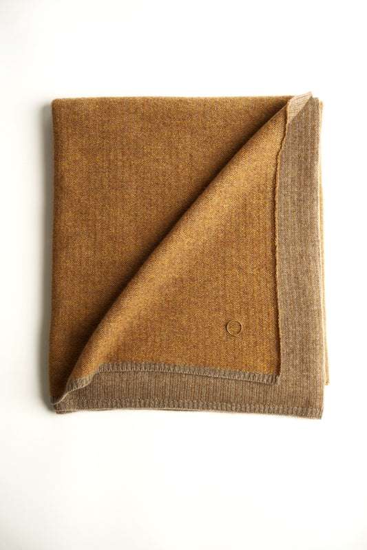 This image features the Letra Throw, a knitted, two-tone float knit throw in a warm, inviting color. The throw displays a soft, textured fabric with a stylish float knit pattern that adds depth and visual interest.