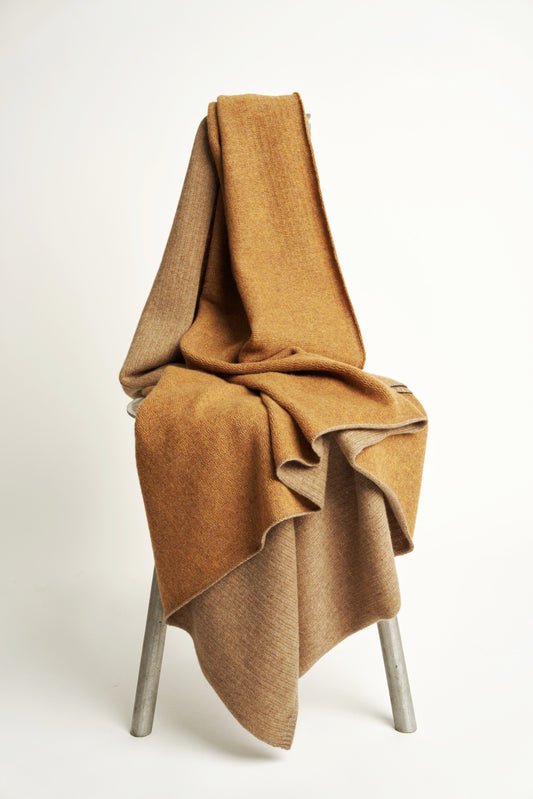 This image features the Letra Throw, a knitted, two-tone float knit throw in a warm, inviting color. The throw displays a soft, textured fabric with a stylish float knit pattern that adds depth and visual interest.