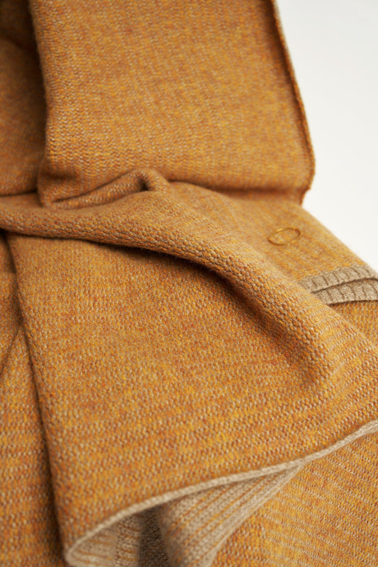 This image features the Letra Throw, a knitted, two-tone float knit throw in a warm, inviting color. The throw displays a soft, textured fabric with a stylish float knit pattern that adds depth and visual interest.