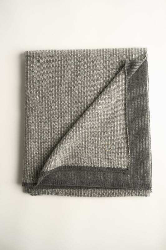 This image features the Letra Throw, a knitted, two-tone float knit throw in a warm, inviting color. The throw displays a soft, textured fabric with a stylish float knit pattern that adds depth and visual interest.