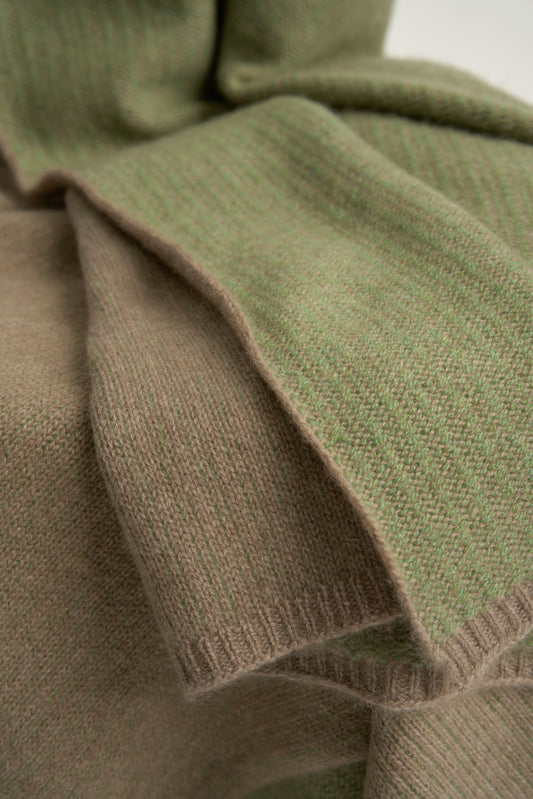 This image features the Letra Throw, a knitted, two-tone float knit throw in a warm, inviting color. The throw displays a soft, textured fabric with a stylish float knit pattern that adds depth and visual interest.