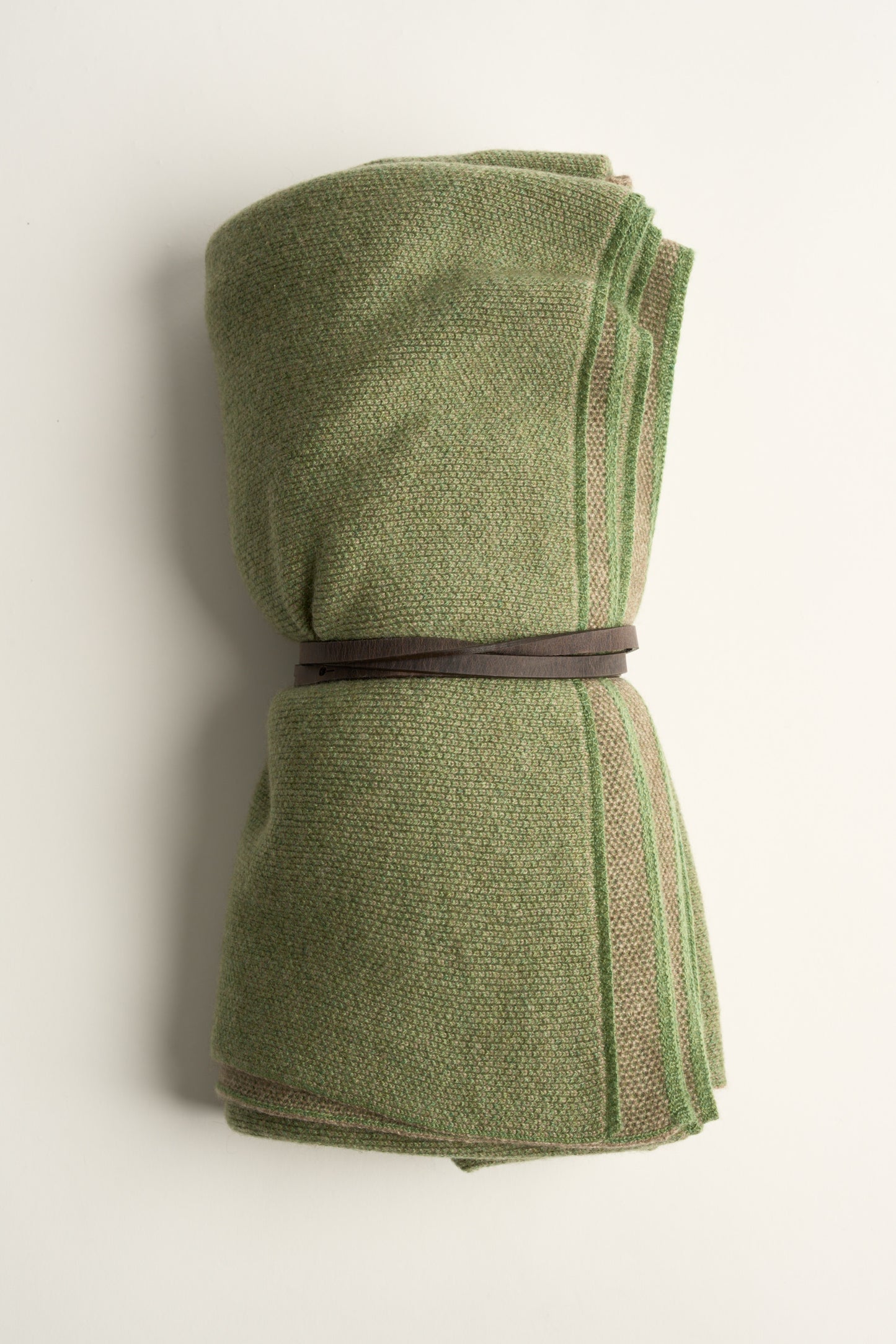 This image displays the Mandu Travel Throw, a luxuriously soft and stylish accessory perfect for enhancing any space. The throw features a delicate, knitted texture in a dual-tone color scheme, with shades of green and subtle taupe.