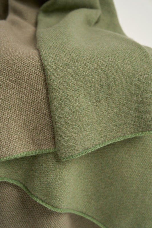 This image features the Mandu Throw, a knitted microfiber throw in a two-tone green & taupe color. The throw displays a soft, textured surface with subtle striping details, enhancing its stylish and cozy appearance.