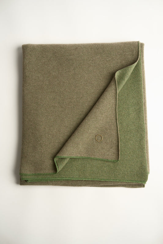 This image features the Mandu Throw, a knitted microfiber throw in a two-tone green & taupe color. The throw displays a soft, textured surface with subtle striping details, enhancing its stylish and cozy appearance.