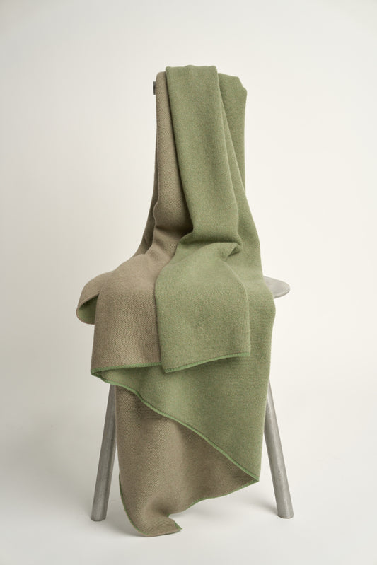 This image features the Mandu Throw, a knitted microfiber throw in a two-tone green & taupe color. The throw displays a soft, textured surface with subtle striping details, enhancing its stylish and cozy appearance.