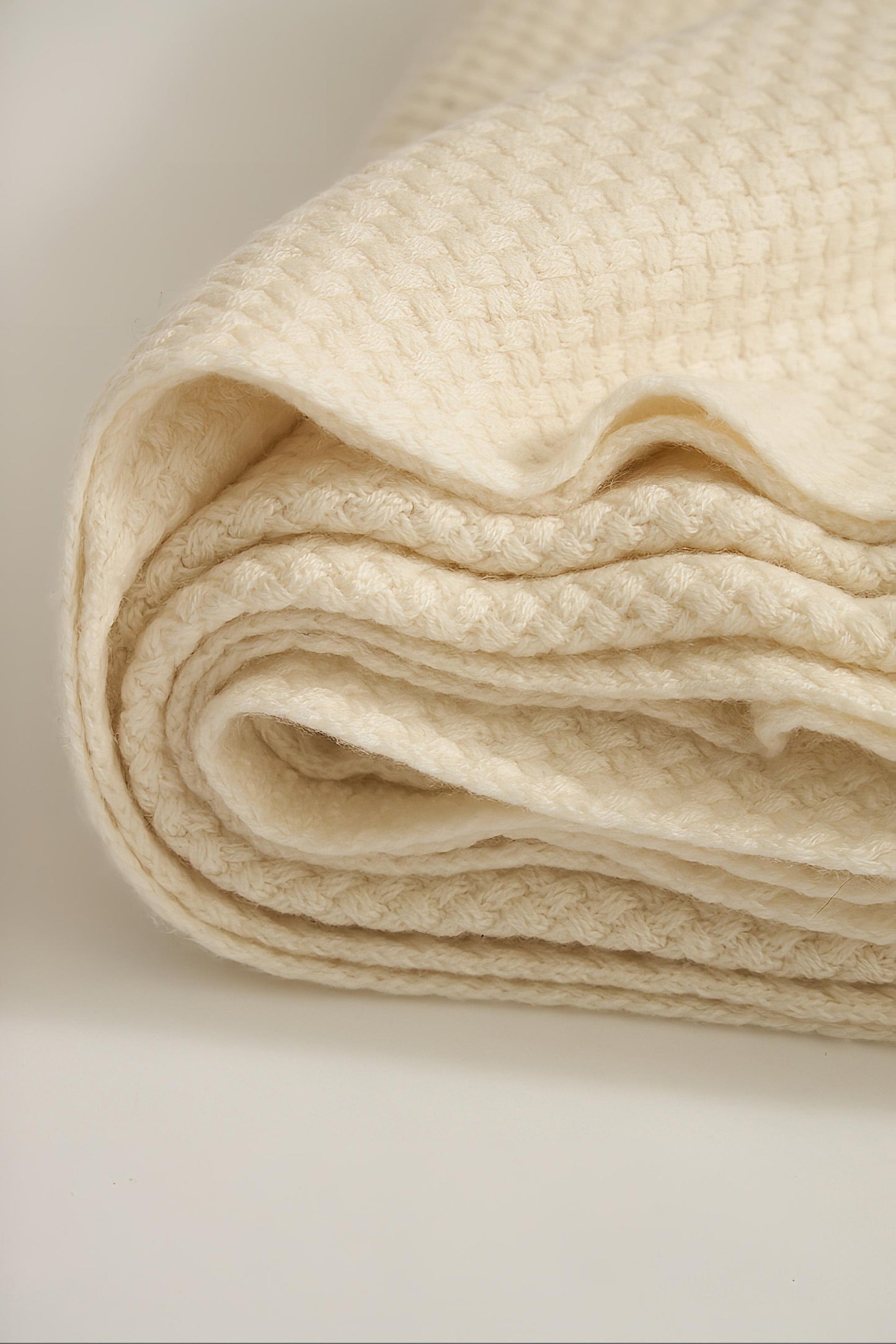 An ivory cashmere bedspread with a subtle pattern, displayed on a neutral background.