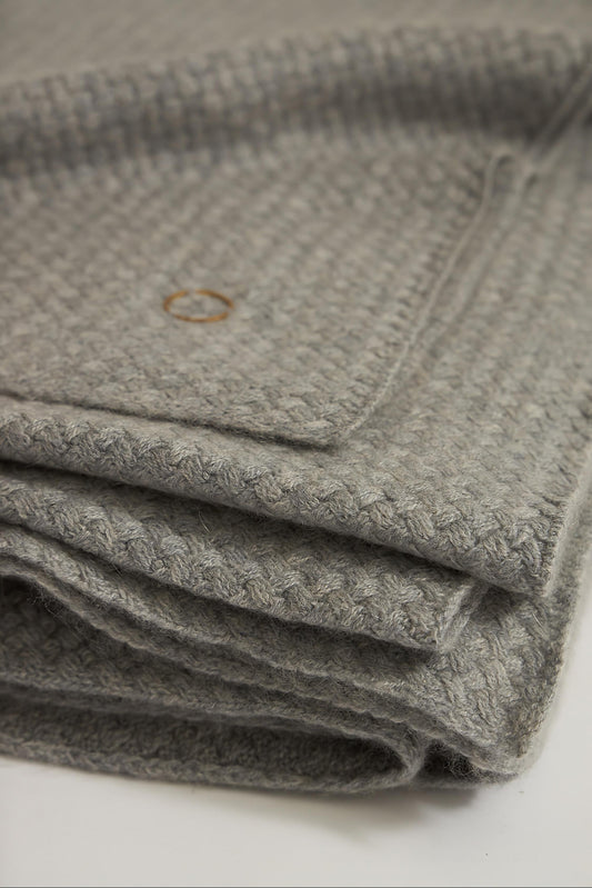 A soft grey cashmere throw with a basket knit pattern, draped over a chair.