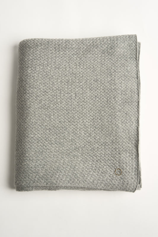 A folded soft grey cashmere bedspread with a subtle pattern, displayed on a neutral background.