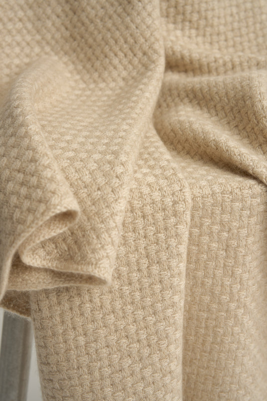 A beige cashmere throw with a basket knit pattern, draped over a chair.