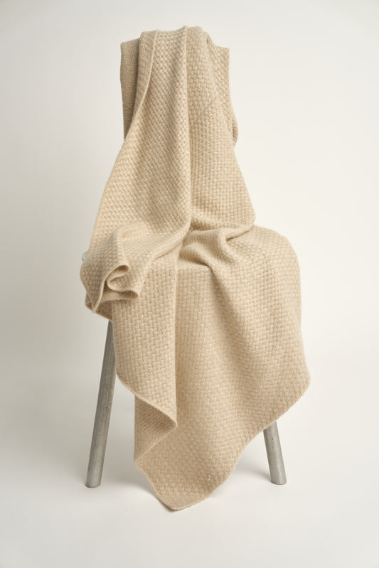 A beige cashmere throw with a basket knit pattern, draped over a chair.