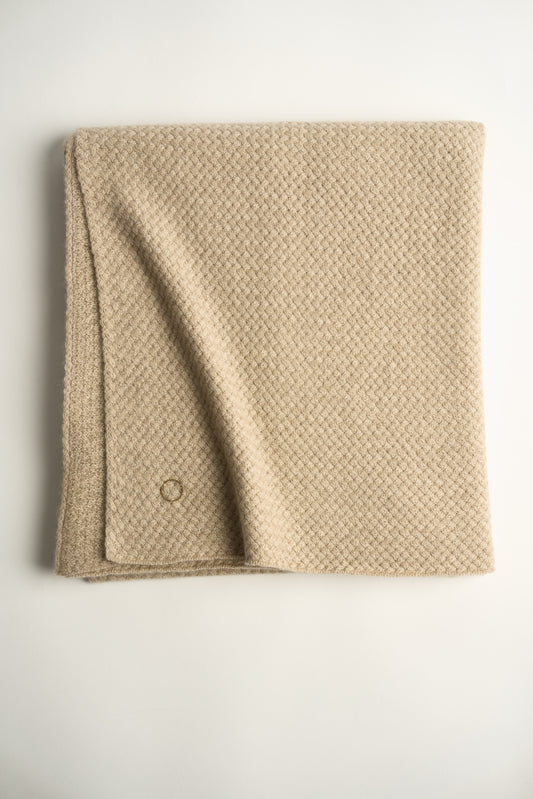 A beige cashmere throw with a basket knit pattern, folded neatly.