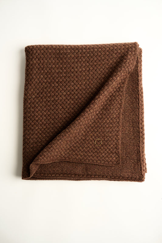 A chocolate cashmere throw with a basket knit pattern, draped and folded on a plain background.