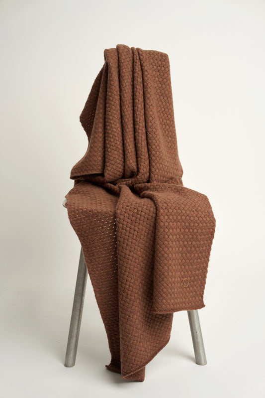 A chocolate cashmere throw with a basket knit pattern, draped over a chair.
