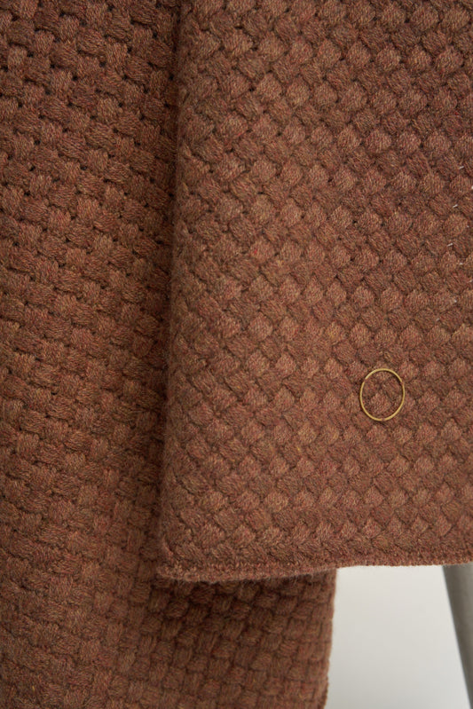 A chocolate cashmere throw with a basket knit pattern, draped over a chair.