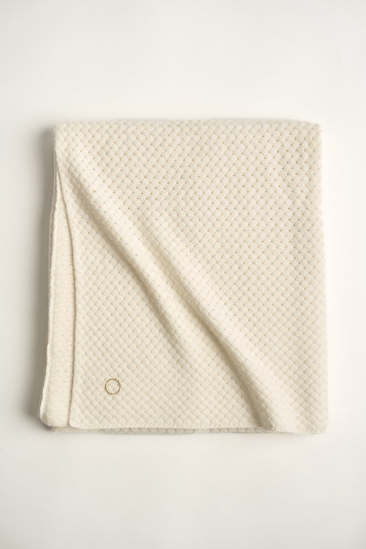 An ivory cashmere throw with a basket knit pattern, neatly folded.