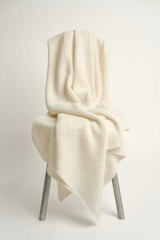 An ivory cashmere throw with a basket knit pattern, draped over a chair.