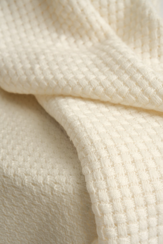 An ivory cashmere throw with a basket knit pattern.