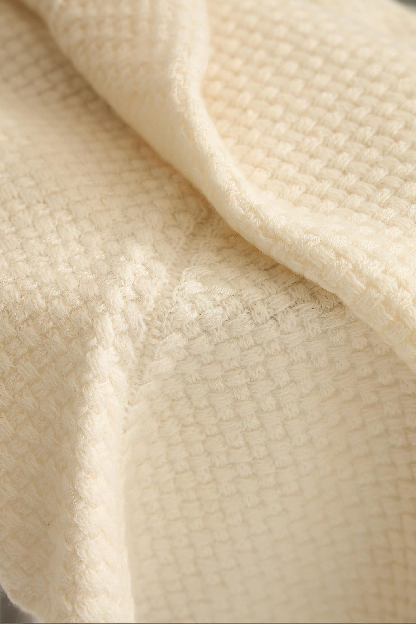 An ivory cashmere bedspread with a subtle pattern, displayed on a neutral background.