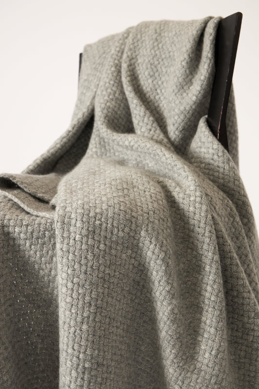 A soft grey cashmere throw with a basket knit pattern, draped over a chair.