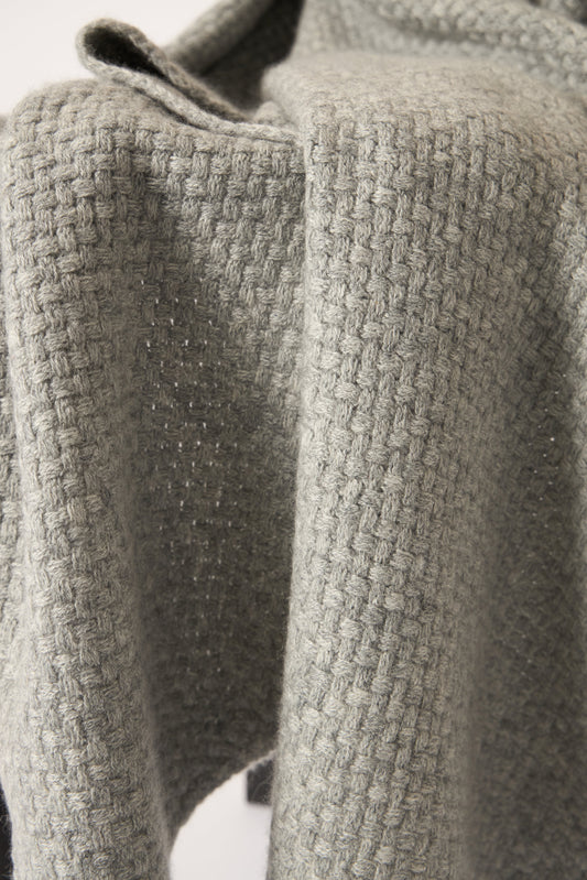 A soft grey cashmere throw with a basket knit pattern, draped over a chair.