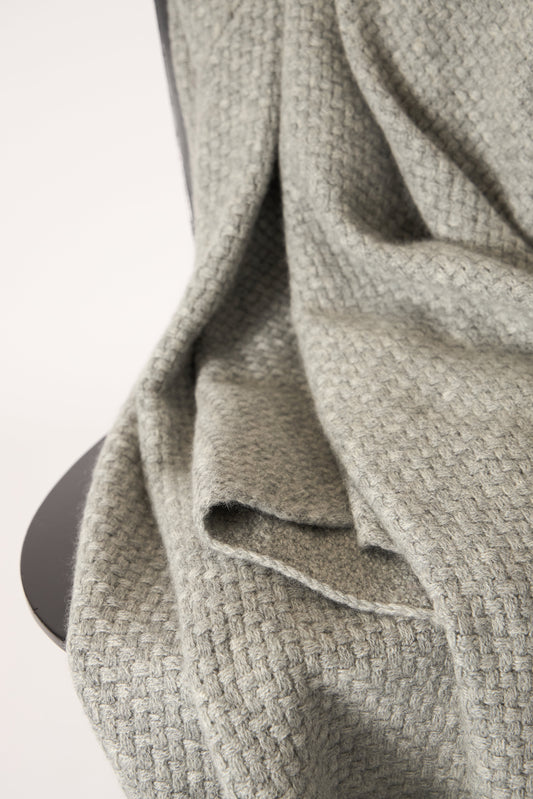 A soft grey cashmere throw with a basket knit pattern, draped over a chair.