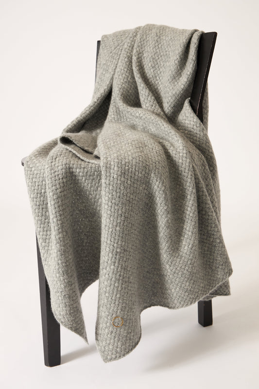 A soft grey cashmere throw with a basket knit pattern, draped over a chair.