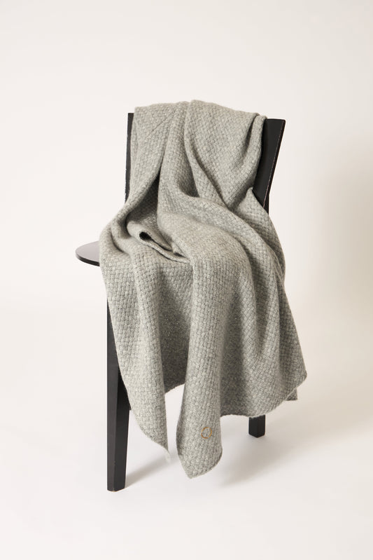 A soft grey cashmere throw with a basket knit pattern, draped over a chair.